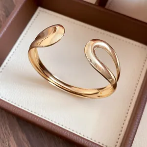 Close-up of gold-plated teardrop open bangle with polished metallic finish and curves.