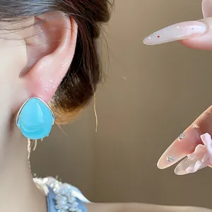 Vista detallada de un pendiente de botón de acrílico azul claro con forma de gota en la oreja