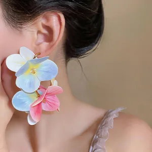 Close-up of model wearing large colorful fabric flower petal earrings in a vacation style.