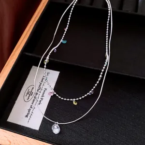 Close-up of a double-layer silver necklace with colorful dangles and a zircon pendant