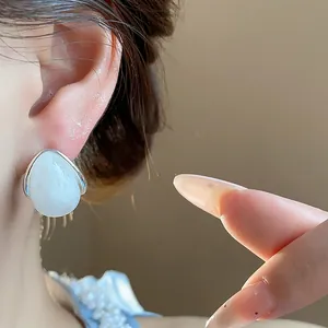 Primer plano de pendientes minimalistas de acrílico blanco en forma de gota en la oreja