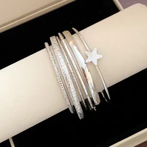 Dettaglio di bracciali rigidi sovrapposti in argento con un charm a forma di stella