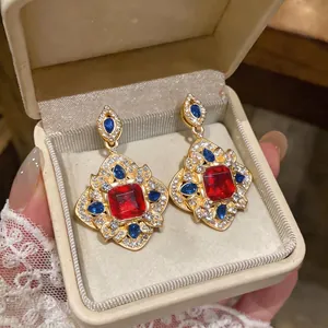 Boucles d'oreilles vintage style cour avec une gemme rouge carrée et des accents bleus.