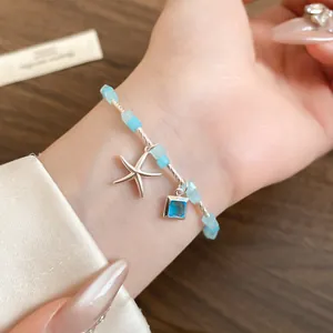 Gros plan d'un bracelet de perles avec breloques étoile de mer et cristal bleu au poignet