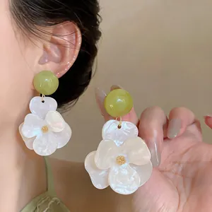 Macro detail of resort style resin flower earrings with white petals and green beads