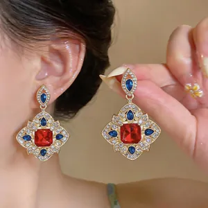 Détail de boucles d'oreilles de style palais vintage avec cristaux rouges et bleus.