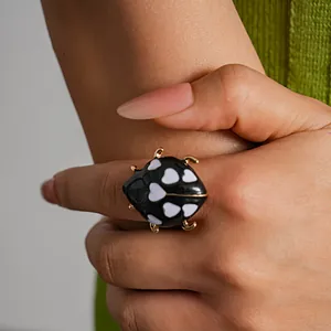Vista dettagliata di un anello coccinella in smalto nero con motivi a cuore sul dito.
