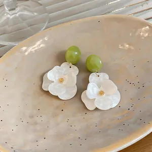 Close-up of elegant resin flower earrings with green beads on a textured ceramic plate.