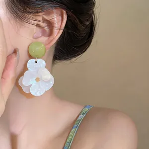 Detailed close-up showing oversized resin flower earrings in white and green on Asian model