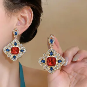 Vue détaillée de boucles d'oreilles losange en or avec pierres précieuses rouges.