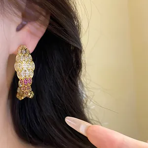 Close-up detail of vintage-style gold fish earring encrusted with red and white zircons.