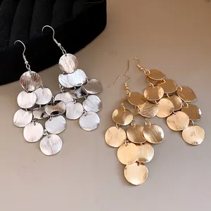 Detail of round geometric tassel earrings in gold and silver brushed metal finishes