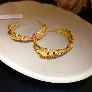 Close-up of vintage C-shaped gold-plated hoop earrings with red and white zircons