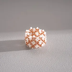 Detailed macro view of a handmade woven ring featuring rose gold and white beads