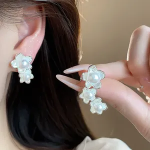 Primo piano di orecchini a fiore asimmetrici con perle, mostrati sull'orecchio e in mano.