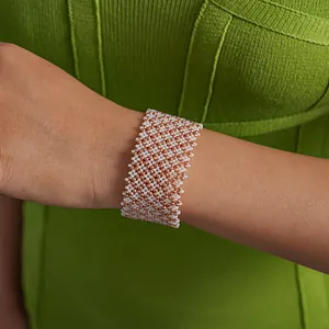 Detailed close-up shot of a wide woven glass bead bracelet in white and rose gold finish.