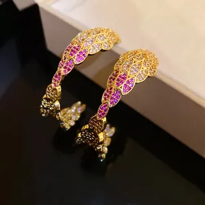Detailed view of C-shaped earrings with white and magenta zircon feather patterns.