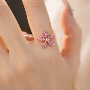 Gros plan d'une bague fleur en or rose avec des cristaux roses étincelants au doigt.