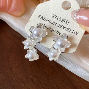 Dettaglio di orecchini a fiore asimmetrici con perle lucide su aghi in argento S925
