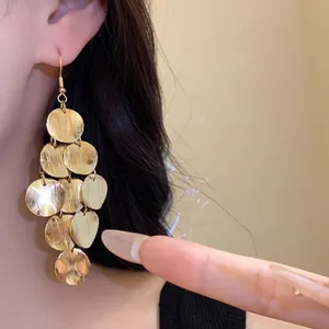 Close-up detail of gold geometric circular tassel drop earrings worn on an ear for style