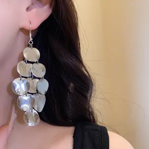 Close-up detail of silver-toned geometric metal disc fringe drop earrings worn by model