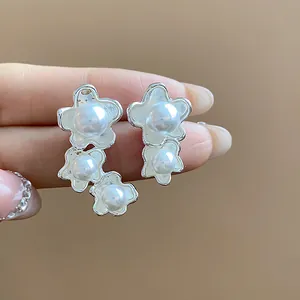 Primo piano di orecchini a fiore d'argento asimmetrici con eleganti perle bianche su fondo beige