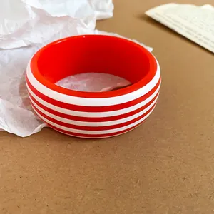 Close-up macro detail of a red and white striped resin bangle on a neutral kraft paper background
