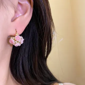 Élégantes boucles d'oreilles créoles fleurs en résine rose sur modèle.