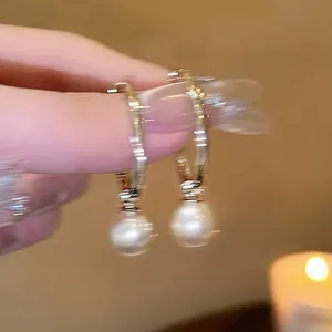 Elegant gold-tone hoop earrings with hanging white pearls on a soft warm background.
