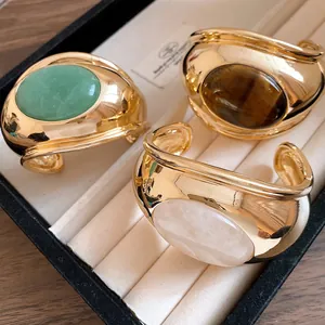 Detail view of three retro chunky gold-tone cuffs featuring tiger's eye and rose quartz stones.