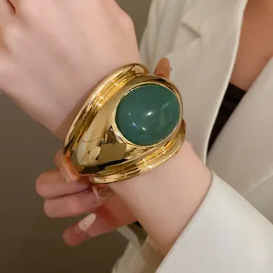 Close-up of vintage gold cuff bracelet with large oval green stone on wrist