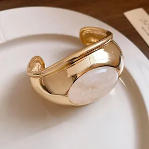 Detailed view of polished gold cuff bracelet featuring a large oval powder crystal stone