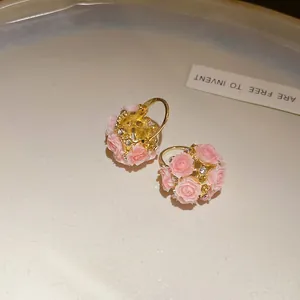 Détail montrant les délicates roses en résine rose et strass sur boucles d'oreilles dorées.