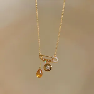 Close-up of gold plated safety pin necklace with star charm and yellow teardrop stone