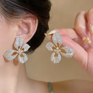 Detailed macro shot of luxury sparkling three-petal flower stud earrings on ear.