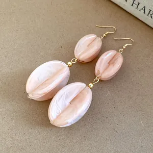 Detailed macro shot of elegant pink marbled acrylic drop earrings with gold bead accents