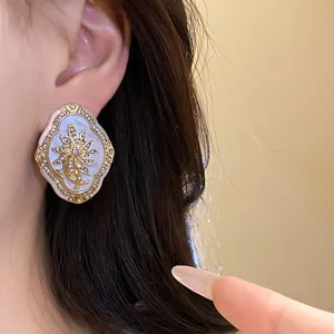 Close-up of vintage floral earring with rhinestones on a white resin base worn on ear.