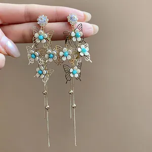 Close-up of elegant gold butterfly and flower dangle earrings with long tassels.