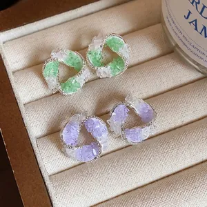 Elegant swirl stud earrings with green and purple glass stones in a jewelry box.