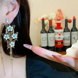 Close-up of elegant gold butterfly tassel earrings with blue flower accents and crystals.