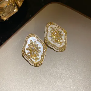 Close-up of vintage gold flower stud earrings with shimmering rhinestones and white inlay.