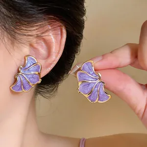 Detail view showing the purple enamel texture and gold edging of the floral stud earrings.