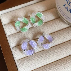 Close-up of swirl design earrings with green and purple glass stones in jewelry tray.