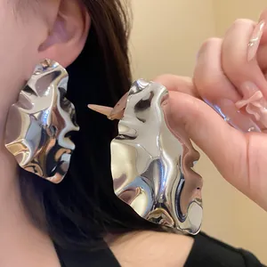 Close-up of silver geometric pleated stud earrings with high-shine metallic finish.