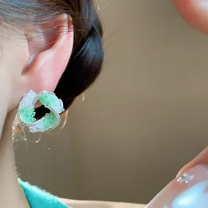 Close-up of elegant vortex stud earrings with green glass and zircon detailing.
