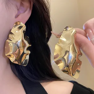 Close-up of oversized gold geometric crumpled stud earrings with a glossy finish