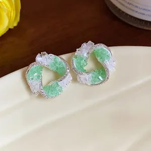 Close-up of elegant silver swirl stud earrings with green and white crushed crystals