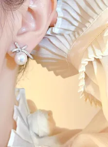 Elegant silver bow earrings with a large white pearl detail shown on a model's ear