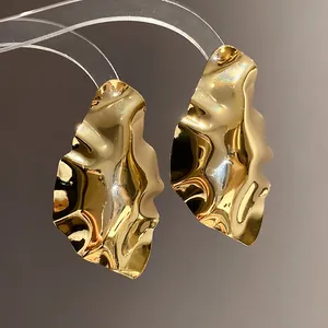 Detail shot of golden crumpled geometric stud earrings with high-shine metallic finish.