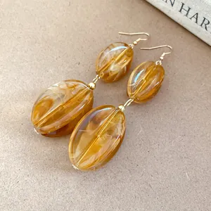Detailed macro view of amber acrylic marble-patterned drop earrings with gold hooks